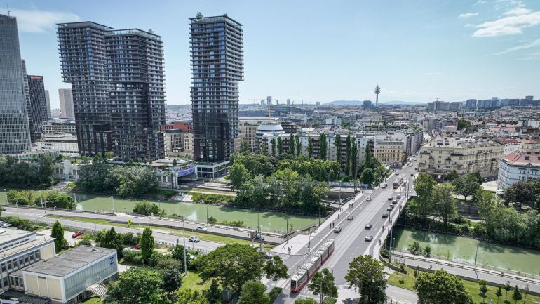 Visualisierung einer breiten Brücke mit Pkw und Straßenbahn, dahinter Stadtgebiet inklusive Skyline