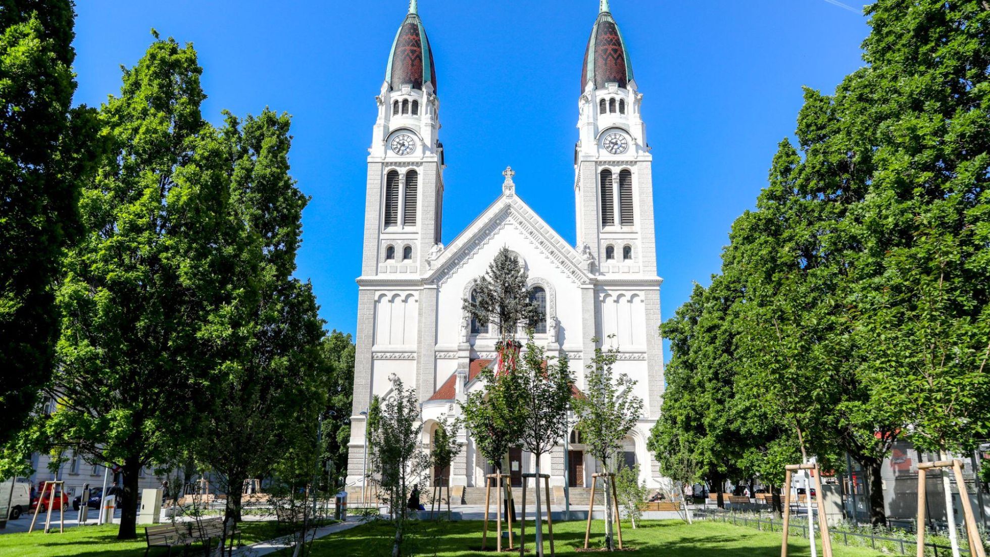 copyright: Stadt Wien / Christian Fürthner Kirche mit Zwillingstürmen, rund herum viele hohe Bäume und Wiese.