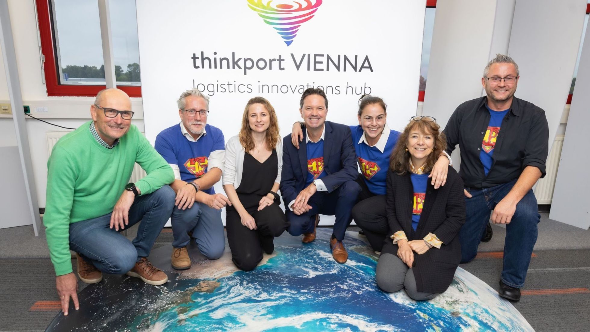 copyright: Monika Fellner Gruppenfoto von Personen auf einer Weltkugel-Abbildung, vor einem Plakat mit Text "thinkport VIENNA".