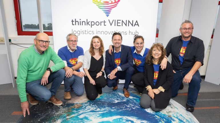 copyright: Monika Fellner Gruppenfoto von Personen auf einer Weltkugel-Abbildung, vor einem Plakat mit Text "thinkport VIENNA".