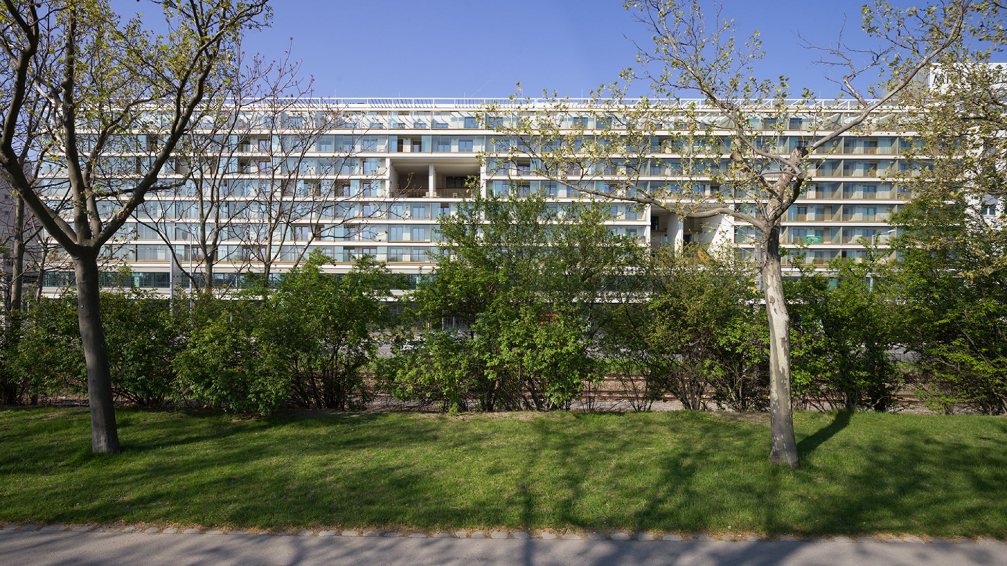 Langer Gebäudekomplex mit verglasten Terrassen, davor Grünflächen