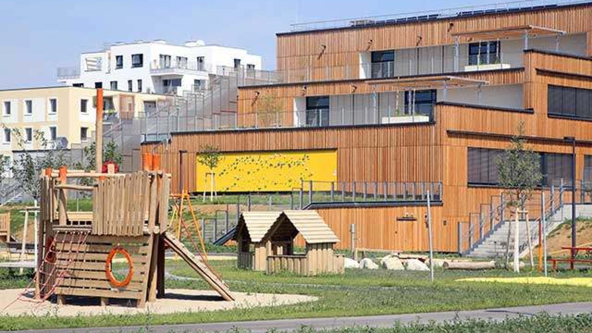 copyright: VOTAVA/PID Ausschnitt des terrassierten Baukörpers. Die Fassade ist mit Holz verkleidet. Davor ist ein Spielplatz.