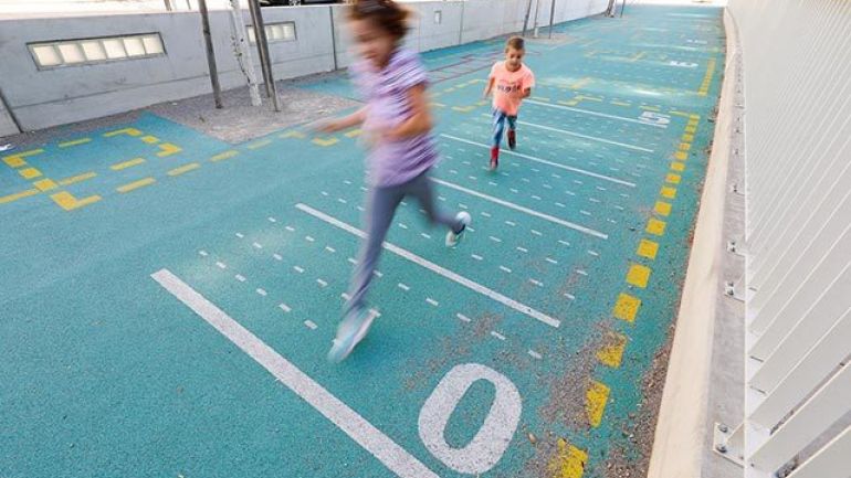 türkis gefärbter Boden, darauf weiße und gelbe Linien, zwei Kinder springen
