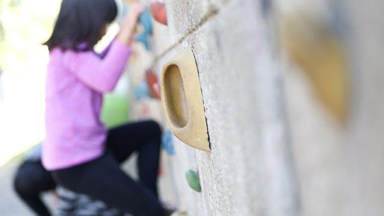 Detailauschnitt, rechts eine Betonwand mit Kletterelementen, im Hintergrund ein kletterndes Kind