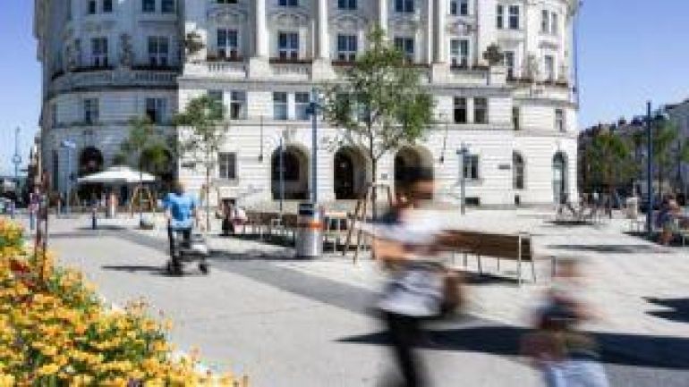 gepflasterste Fläche mit Sitzbänken, im Vordergrund Blumen, im Hintergrund hisstorisches Gebäude