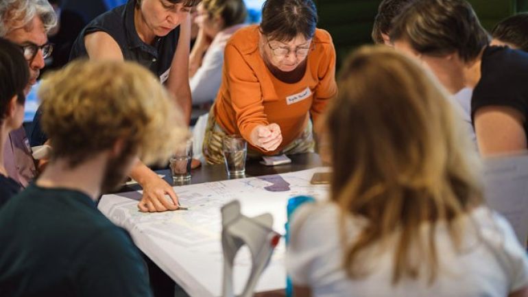 Menschen rund um einen Tisch beugen sich über einen Straßenplan und diskutieren Potentiale für eine Umgestaltung des öffentlichen Raums