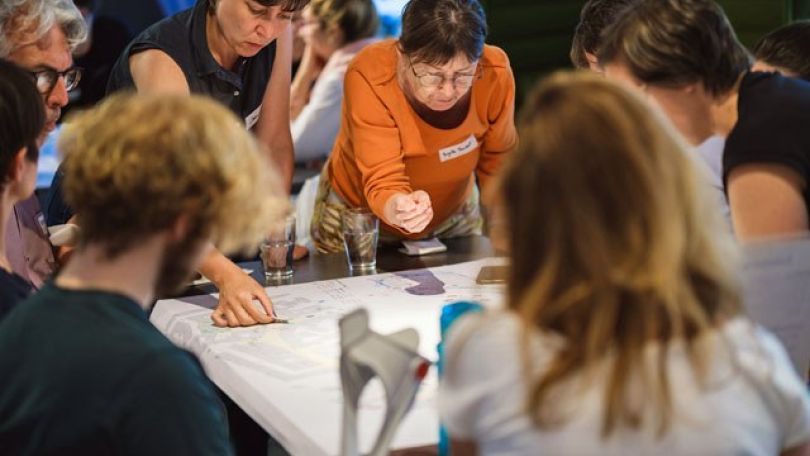 Menschen rund um einen Tisch beugen sich über einen Straßenplan und diskutieren Potentiale für eine Umgestaltung des öffentlichen Raums