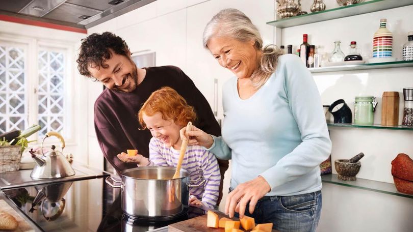 Ein Mann, ein Kind und eine Frau kochen an einem neuen Herd Gemüse.