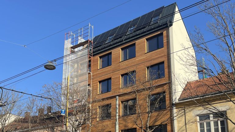 Gebäude mit Holzfassade, seitlich einem Gerüst und Solar-Paneelen am Dach