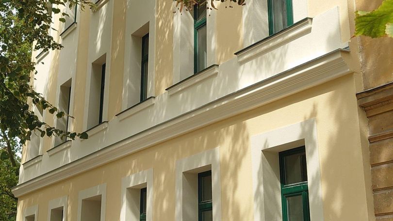 Fassade eines Gründerzeithauses, im oberen Bildrand sind Blätter eines Baumes.
