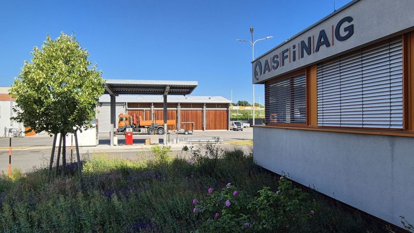 Blick auf Betriebsgelände mit Gebäuden, Fahrzeugen, Tanksäule und Grünfläche.