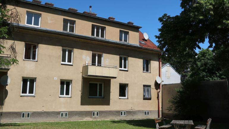 Fassade einer Wohnhausanlage mit Wiese und Sitzmöbeln