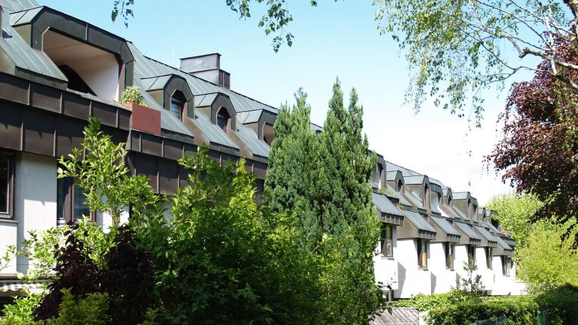 Wohnhausanlage, im Vordergrund Gärten mit Pflanzen und Zäunen