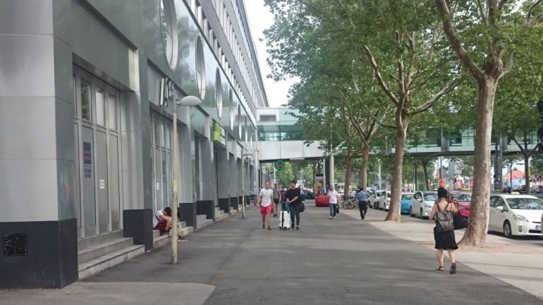 Breiter Gehweg mit Baumallee neben Einkaufszentrum