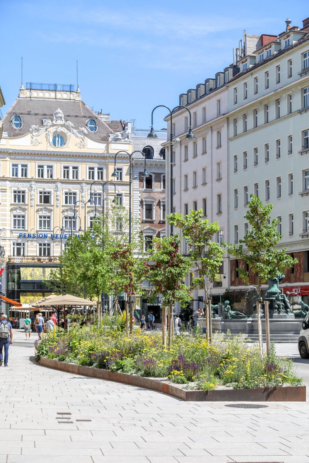 Neuer Markt mit Platanen und Staudensträuchern, in Granit und erhöhte Baumscheiben eingefasst, dahinter der sanierte Donnerbrunnen sowie Passant*innen