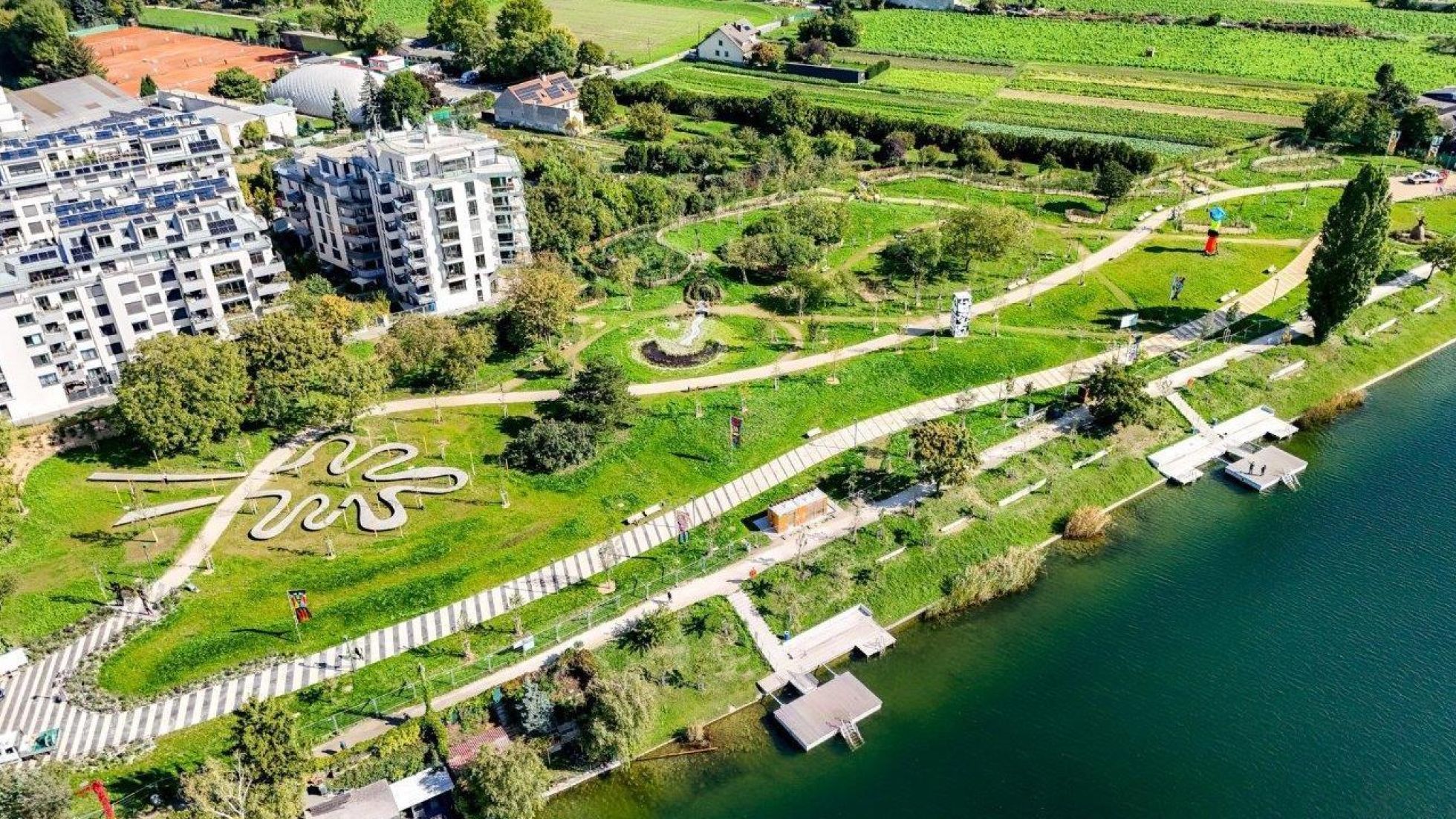 Grünes Areal mit Wegen und Kunst-Stationen am Wasser, am Ufer sind Stege und Holzplattformen.