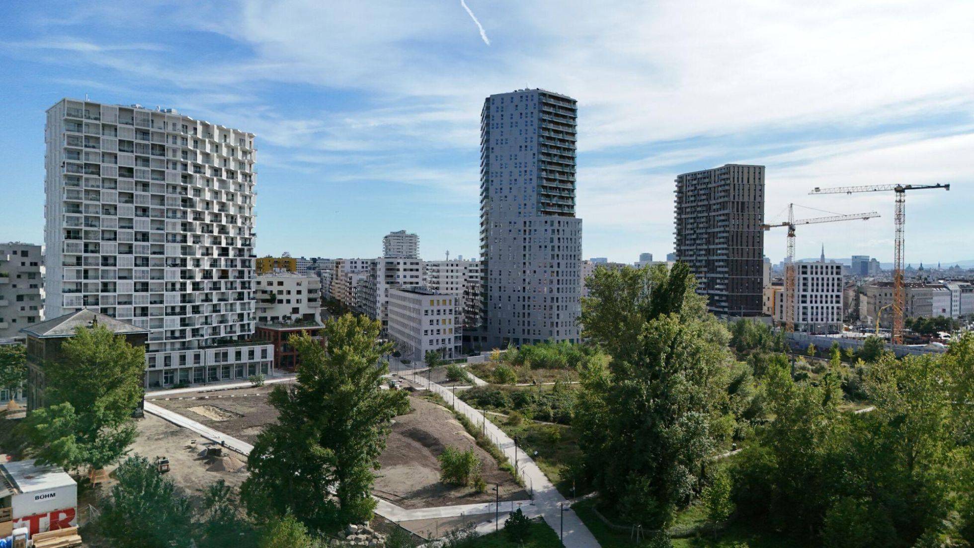 Wohngebäude, teils Hochhäuser, davor Grünfläche mit Bäumen und Skatepark.