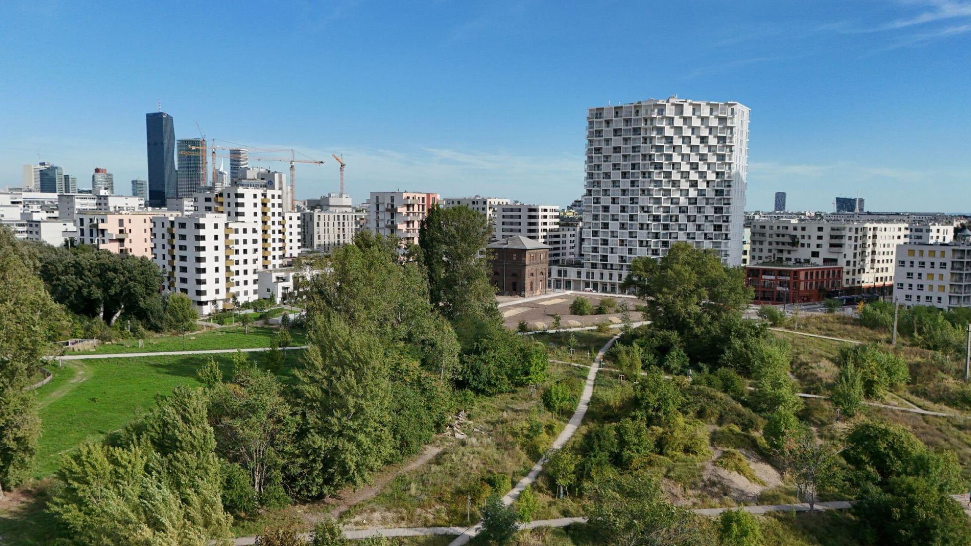 Moderne, unterschiedlich hohe Gebäude, davor eine Grünfläche mit Gehwegen.