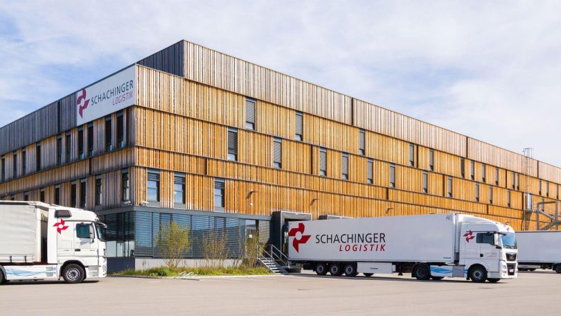 Vor einer großen Produktioshalle mit moderner Holzfassade parkt ein Lkw zum Ein- und Ausladen.
