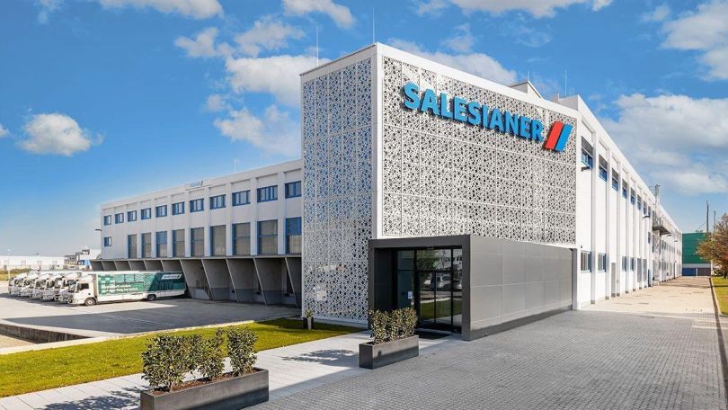 copyright: Salesianer Modernes Firmengebäude mit heller Fassade. An einer Seite des Gebäudes parken mehrere Lkws zum Ein- und Ausladen.