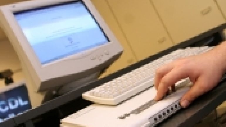 Hand tastet über Braillezeile, im Hintergrund Bildschirm und Tastatur