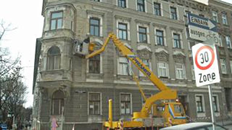 Einsatzwagen mit Hebearm vor Haus mit schadhafter Fassade