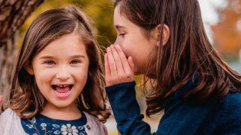 Ein Mädchen flüstert einem anderen Mädchen etwas ins Ohr