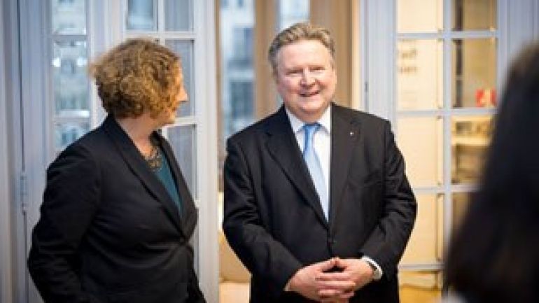 Frau in schwarzem Blazer neben Mann in Anzug mit verschränkten Händen