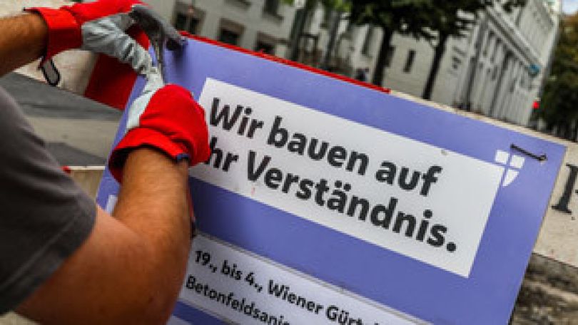 Arbeiter bringt eine Baustelleninformation an