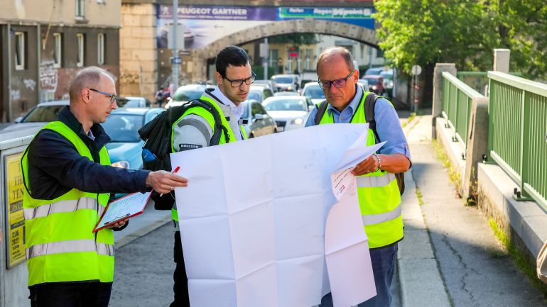 3 Männer in Warnwesten schauen auf einen Plan
