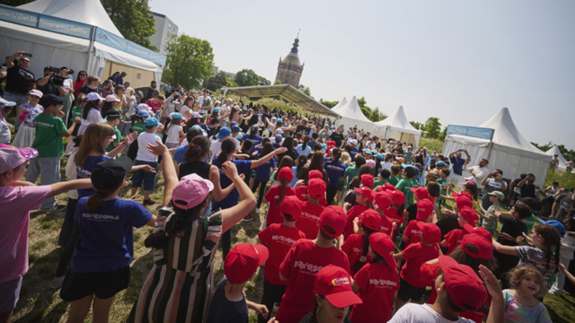 Viele Kinder stehen und tanzen auf der Wiese vor dem Wasserturm.