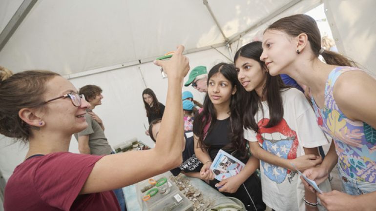 Kinder basteln in einem großen Zelt, von der Decke hängen die Stoff-Maskottchen Tim und Trixi (2 Wassertropfen mit Gesicht)