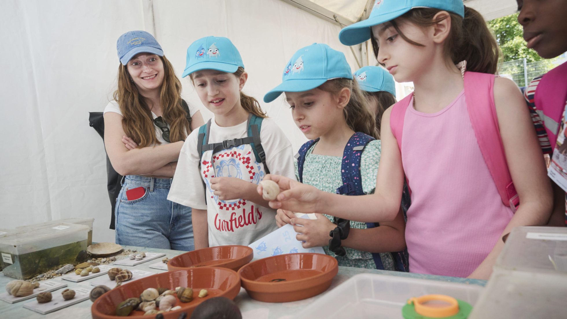 Mehrere Mädchen begutachten verschiedene Schneckenhäuser. Alle tragen eine blaue Kappe vom Wasserfest.