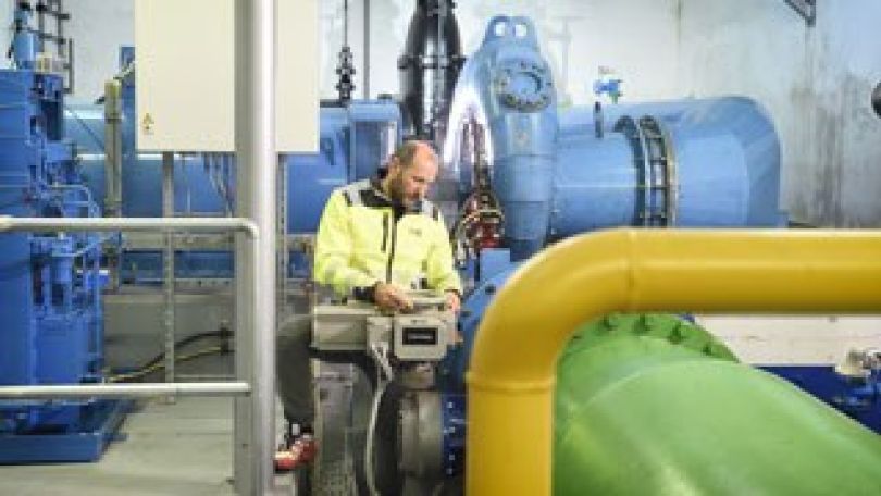 Ein Mitarbeiter kontrolliert technische Anlagen in einem Wasserwerk mit großen blauen Rohren und Ventilen.