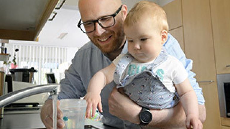 copyright: Wiener Wasser/Zinner Mann mit Baby auf dem Arm füllt eine Trinkflasche am Wasserhahn