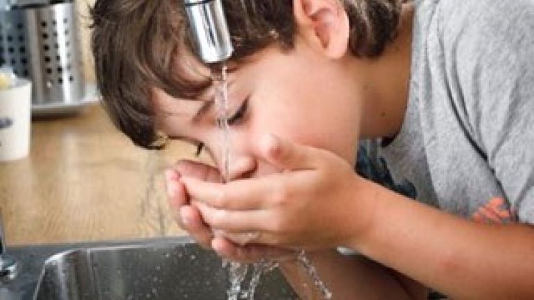 Bub trinkt Wasser aus Wasserhahn