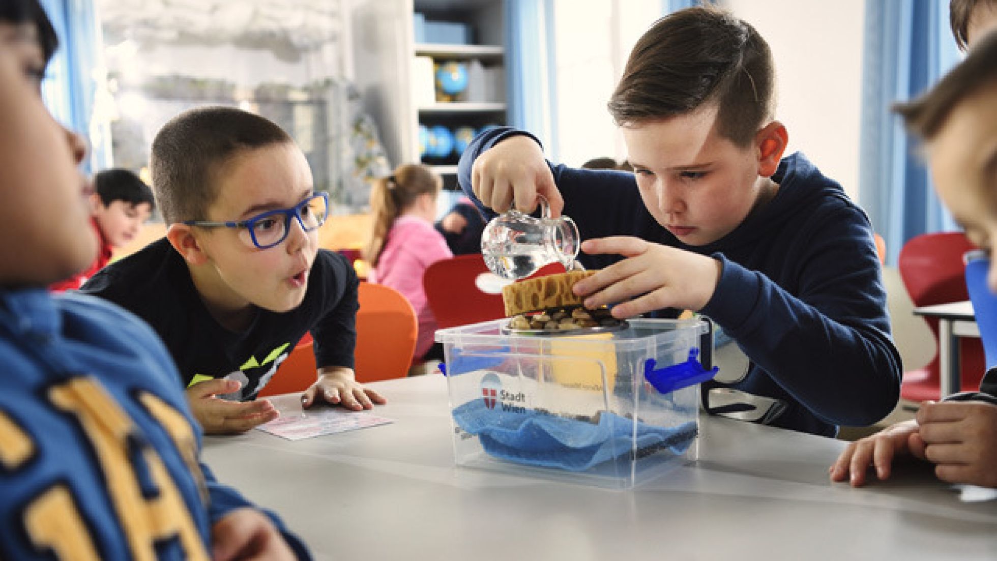 Ein Junge leert Wasser auf einen Schwamm, 3 andere Jungen sehen dabei zu