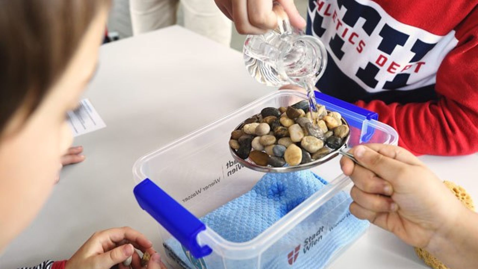 Schüler leert Wasser über einen Teller voller Steine