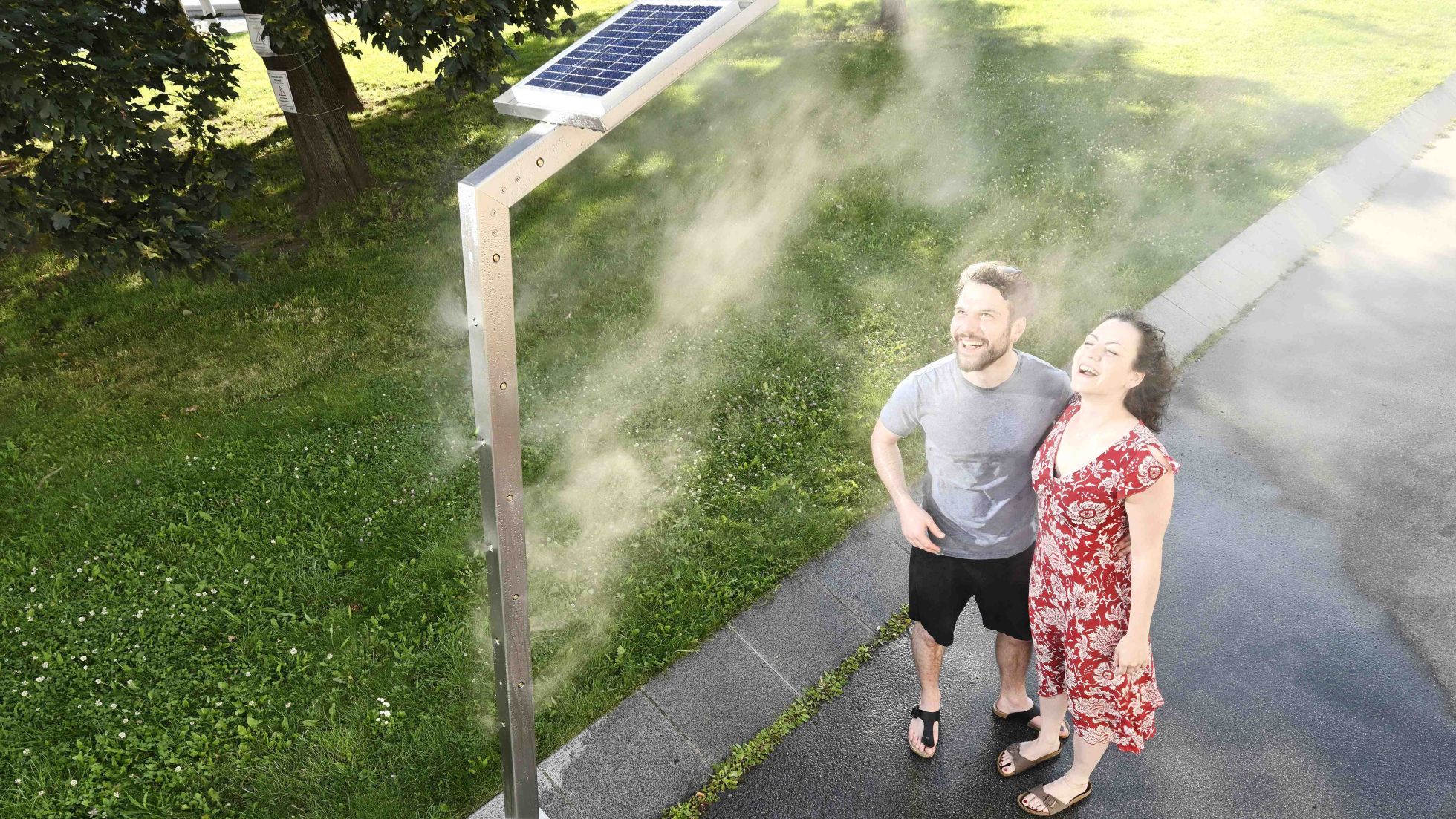 2 Personen stehen in Sommerkleidung unter einer Nebelsteele und kühlen sich ab.