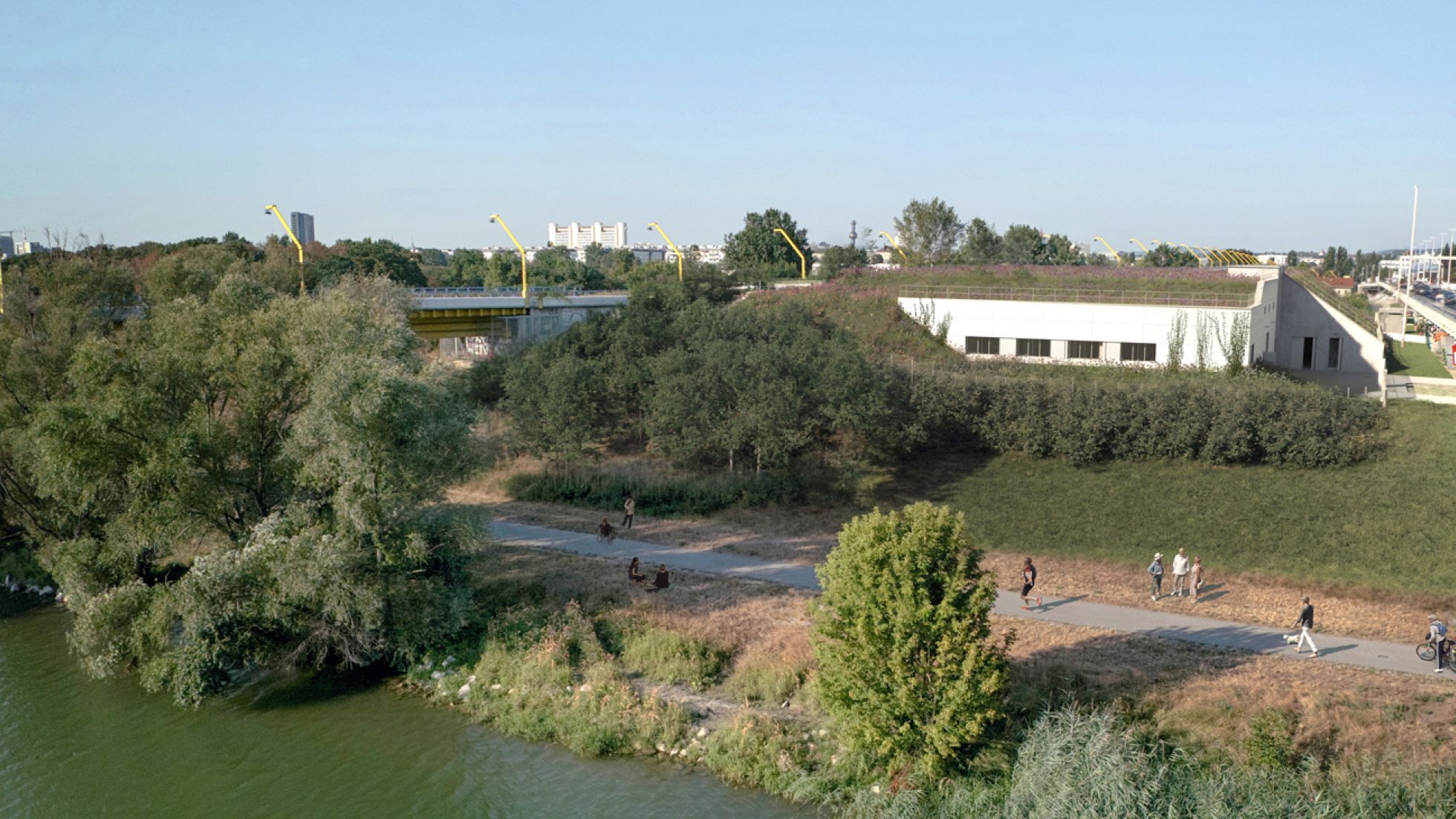 copyright: Stadt Wien/convex/Pulse/Illichmann/Janusch Zwischen 2 Brücken auf der Donauinsel steht ein niedriges weißes Gebäude mit begrüntem Dach. Davor wachsen Sträucher. Am Gehweg am Ufer spazieren Menschen.