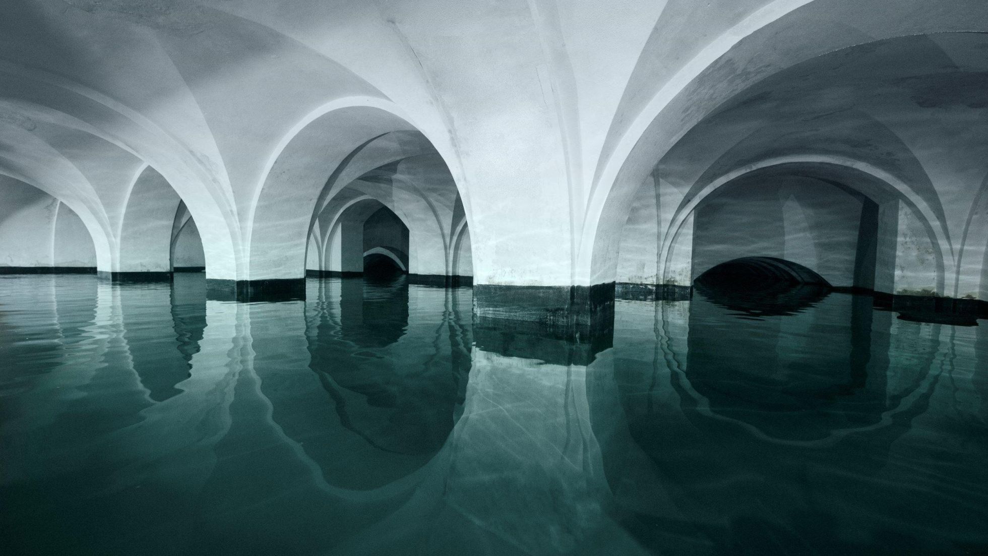 copyright: Vienna Water - Novotny Underground water reservoir with white vaulted arches reflected in still water.
