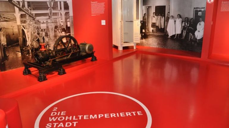 Roter Ausstellungsraum mit Schriftzug "Die wohltemperierte Stadt" am Boden