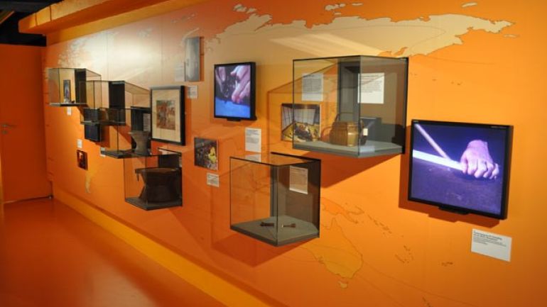 Orange Wand mit Ausstellungsstücken in Vitrinen