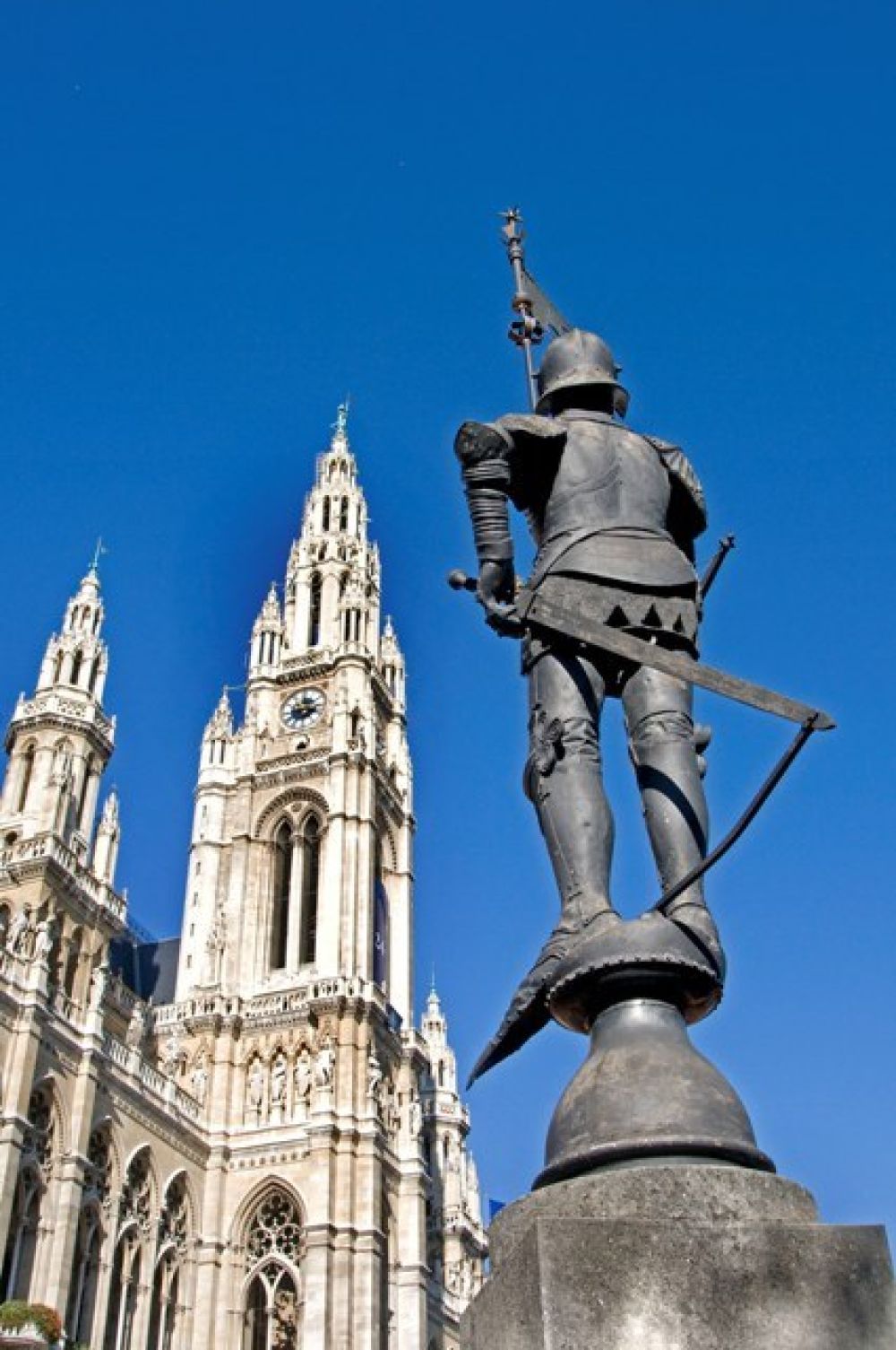 Rathausturm unter blauem Himmel, im Vordergrund eine Statue von hinten