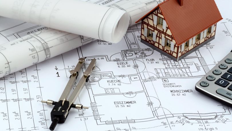 copyright: Bilderbox.com Bauplan, darauf ein Zirkel, ein Taschenrechner, Papierrollen und ein Miniaturhaus