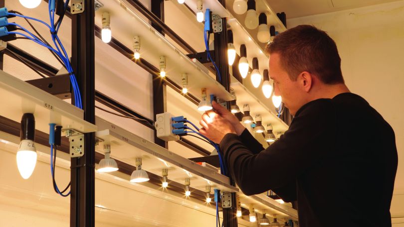 Mitarbeiter schraubt Leuchtmittel in Anlage zur Leuchtenprüfung