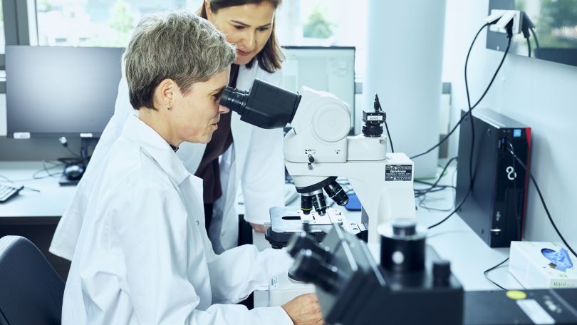 copyright: Michael Rausch-Schott Arbeit im Wasserlabor. Eine Mitarbeiterin sitzt am Mikroskop. Eine zweite Mitarbeiterin steht neben ihr.