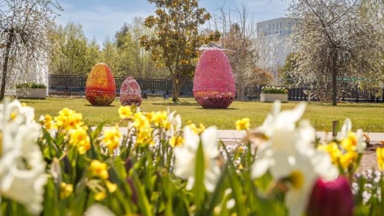 3 große Ostereier aus Metalldraht in einer Wiese, davor ein Blumenbeet