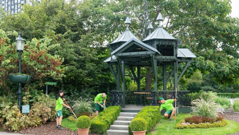 copyright: Wiener Stadtgärten/Zupanc 3 Personen in grüner Arbeitskleidung pflegen die Wiese neben einem Pavillon