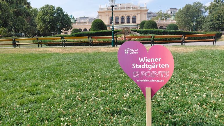 copyright: Wiener Stadtgärten (MA 42) Kleines Schild ins Herzform mit Text "Wiener Stadtgärten - 12 points" steckt in einer Wiese vor einem historischen Gebäude.